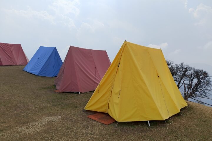 Yellow, red and blue camping tents pitched on a grassy hill under a cloudy sky