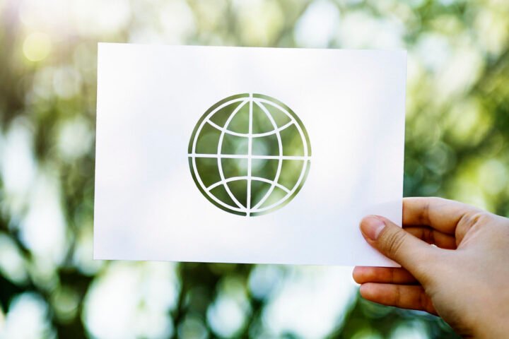 A hand holding a paper printed with a map of the world