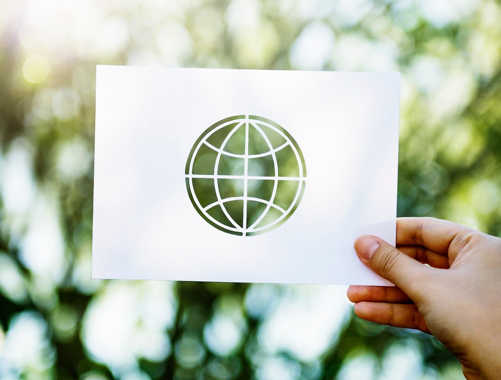 A hand holding a paper printed with a map of the world