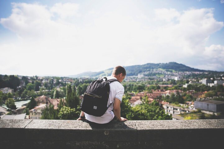 A man with a backpack sitting on a ledge overlooking a city