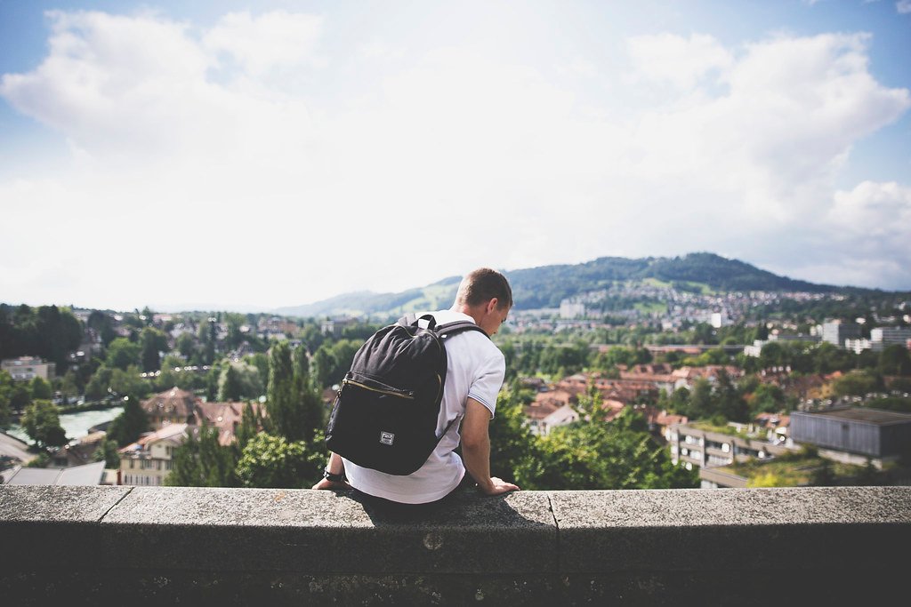 A man with a backpack sitting on a ledge overlooking a city