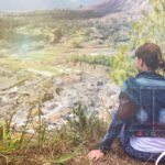 Young woman with a backpack sitting on a rock and looking toward the horizon on Mount Batur, Bali