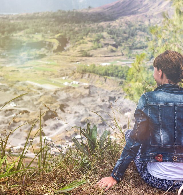Young woman with a backpack sitting on a rock and looking toward the horizon on Mount Batur, Bali