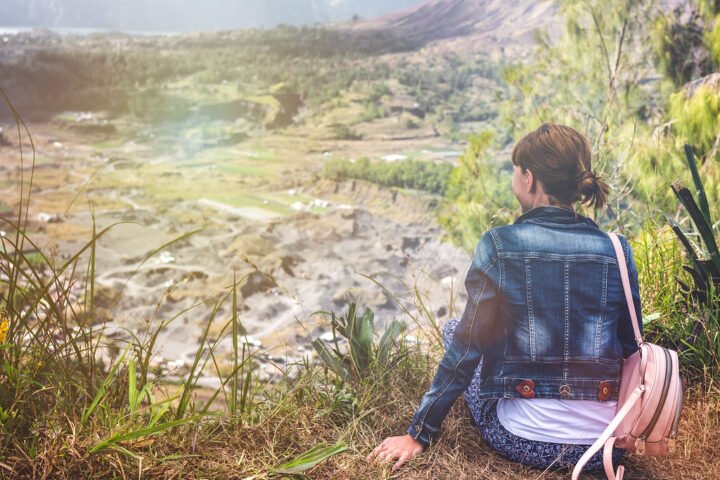 Young woman with a backpack sitting on a rock and looking toward the horizon on Mount Batur, Bali