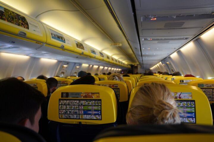 View of an airplane cabin from the back with rows of yellow seats and passengers