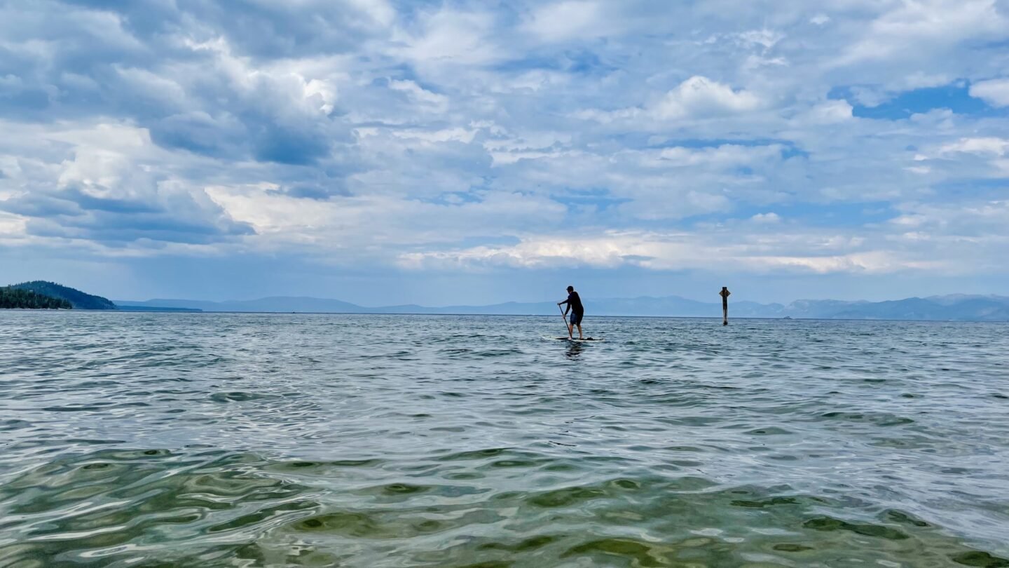 A person stand-up paddleboarding on the rippling water of Lake Tahoe under a cloudy sky, with mountains on the horizon