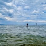 A person stand-up paddleboarding on the rippling water of Lake Tahoe under a cloudy sky, with mountains on the horizon