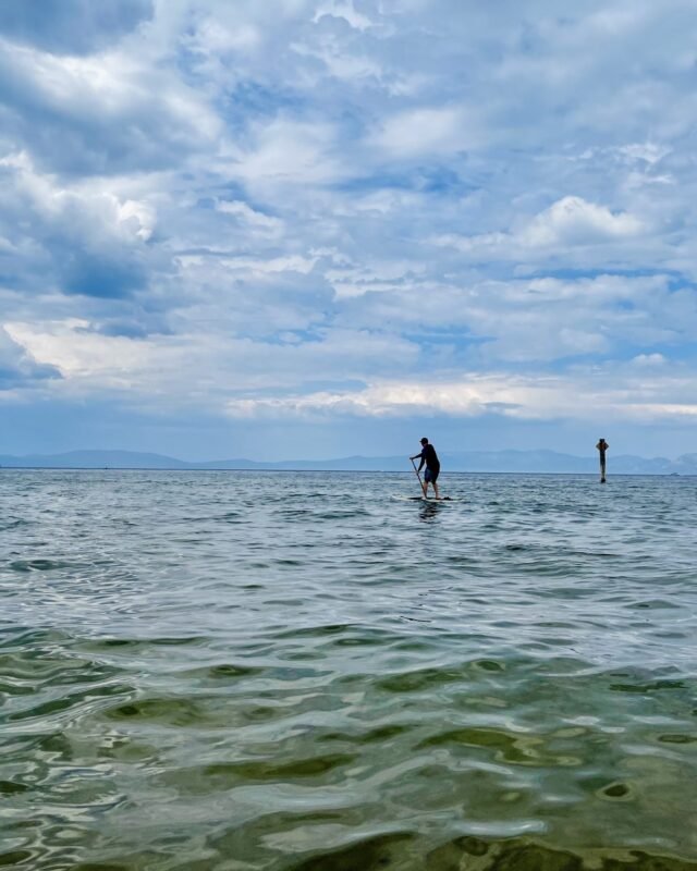 A person stand-up paddleboarding on the rippling water of Lake Tahoe under a cloudy sky, with mountains on the horizon