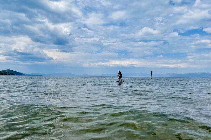 A person stand-up paddleboarding on the rippling water of Lake Tahoe under a cloudy sky, with mountains on the horizon