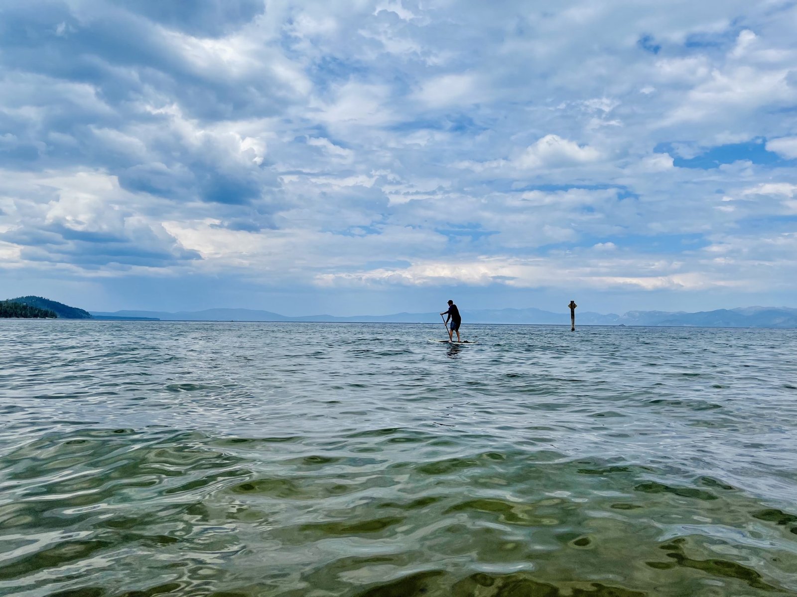 A person stand-up paddleboarding on the rippling water of Lake Tahoe under a cloudy sky, with mountains on the horizon