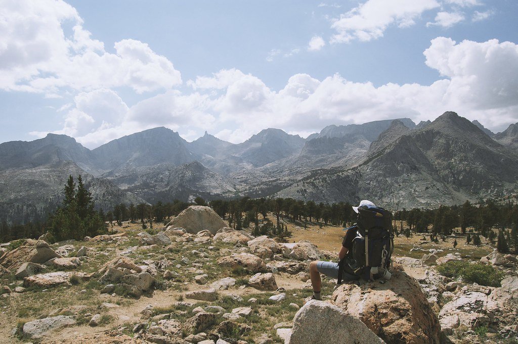 A hiker with a backpack sitting on a rock overlooking mountains